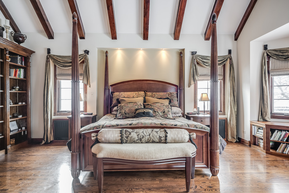 Modelo de dormitorio principal tradicional grande con paredes beige, suelo de madera en tonos medios, todas las chimeneas, marco de chimenea de madera y suelo marrón