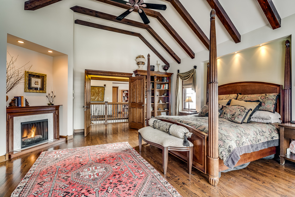 Modelo de dormitorio principal clásico grande con paredes beige, suelo de madera en tonos medios, todas las chimeneas, marco de chimenea de madera y suelo marrón