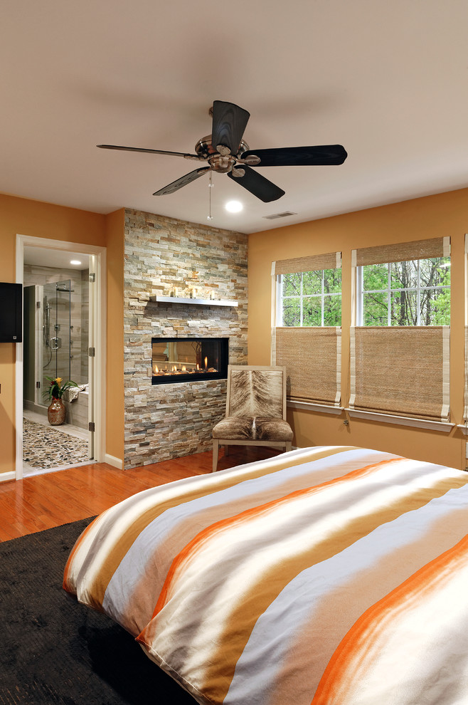Foto de dormitorio principal tradicional renovado de tamaño medio con parades naranjas, suelo de madera en tonos medios, marco de chimenea de piedra, chimenea de doble cara y suelo naranja