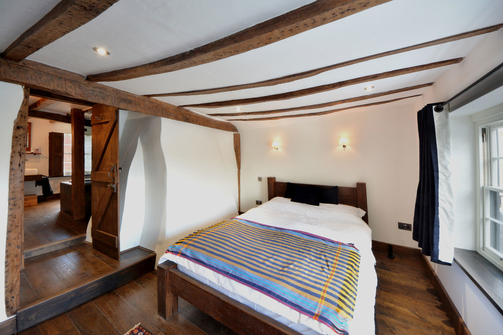 Modelo de dormitorio principal campestre de tamaño medio sin chimenea con paredes blancas y suelo de madera oscura