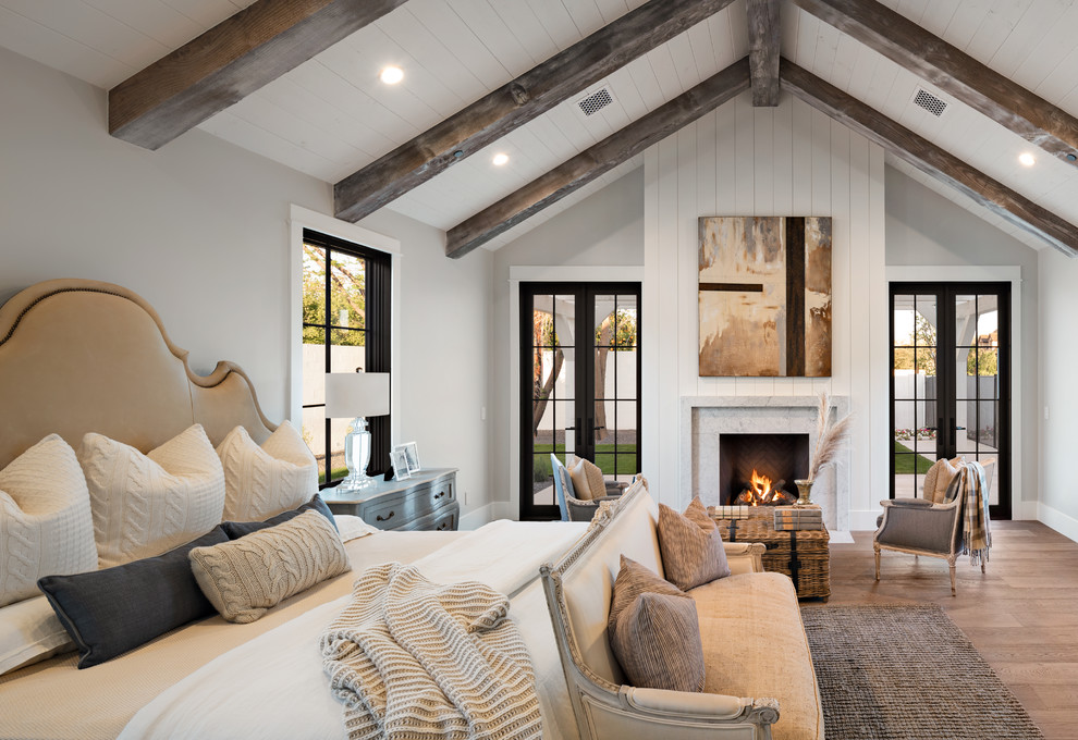 Cette image montre une chambre rustique avec un mur gris, un sol en bois brun, une cheminée standard, un manteau de cheminée en pierre et un sol marron.