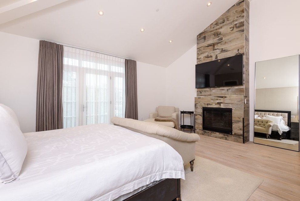 Modelo de dormitorio principal tradicional renovado grande con paredes blancas, suelo de madera clara, todas las chimeneas, marco de chimenea de madera y suelo beige