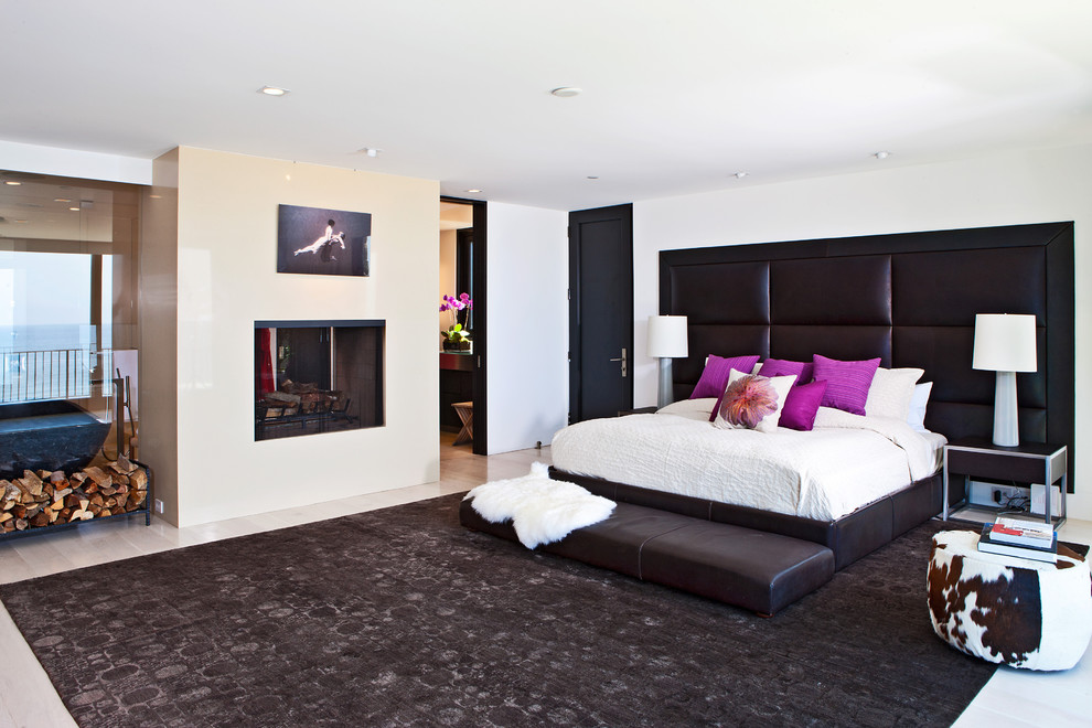 Geräumiges Modernes Hauptschlafzimmer mit weißer Wandfarbe, hellem Holzboden, Kaminumrandung aus Stein und Tunnelkamin in Los Angeles