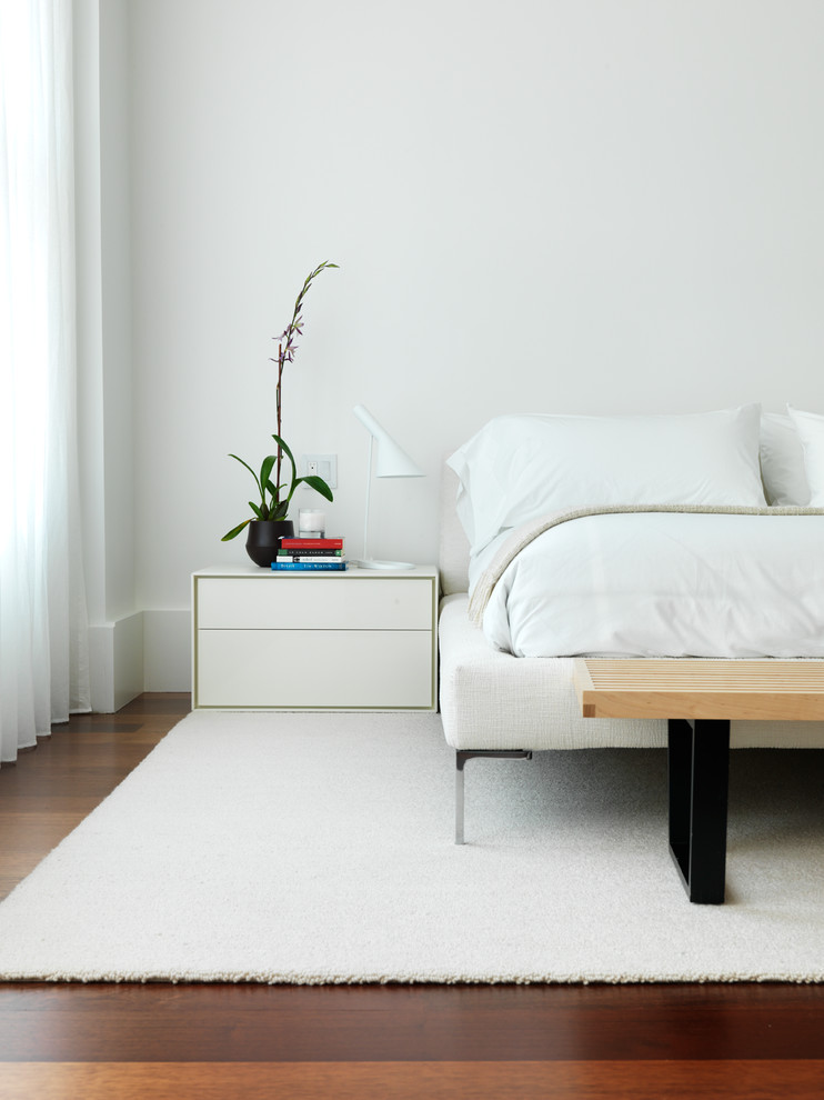 Contemporary bedroom in New York with white walls and medium hardwood flooring.