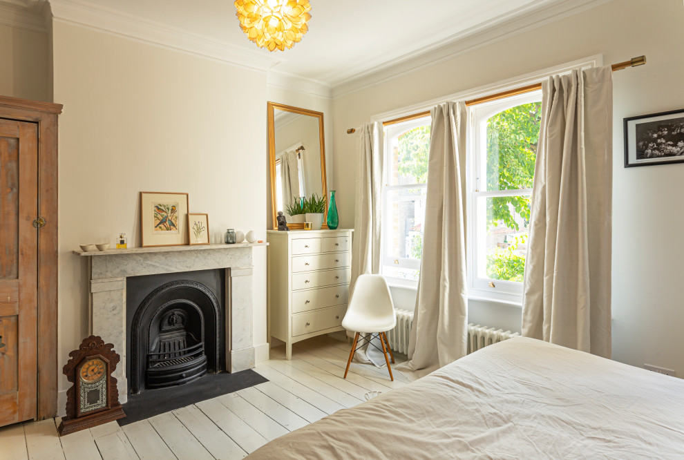 Klassisk inredning av ett sovrum, med beige väggar, målat trägolv, en standard öppen spis och vitt golv