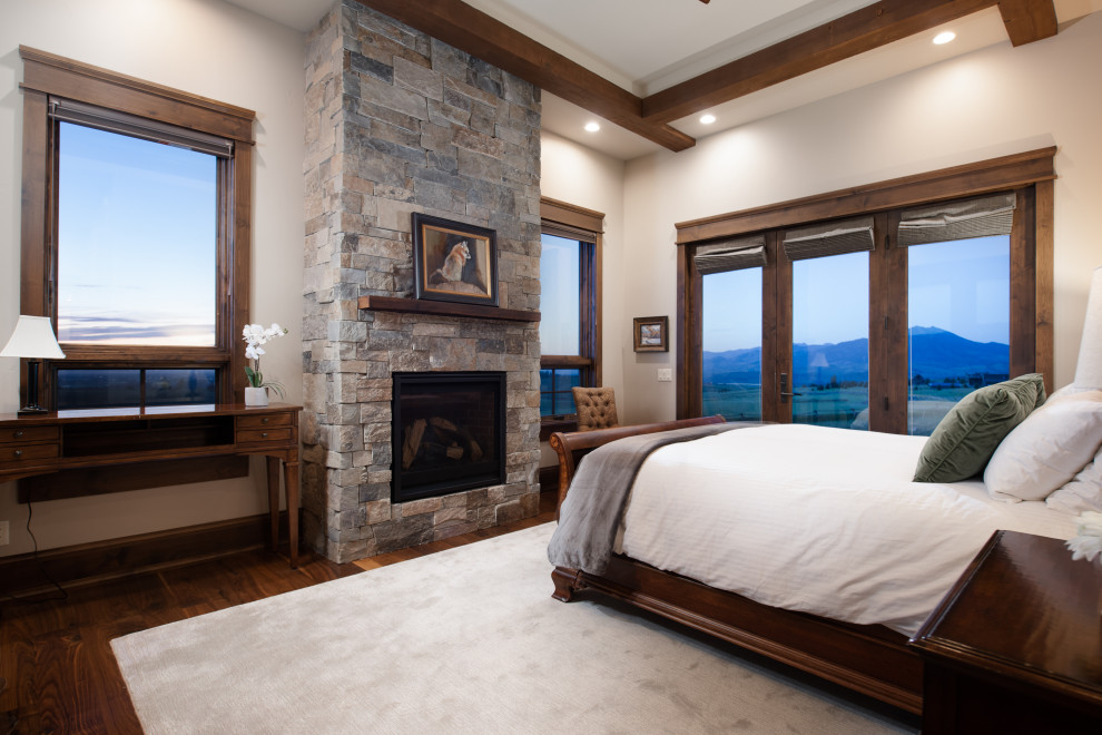 Mountain style master dark wood floor and exposed beam bedroom photo in Other with beige walls, a standard fireplace and a stone fireplace