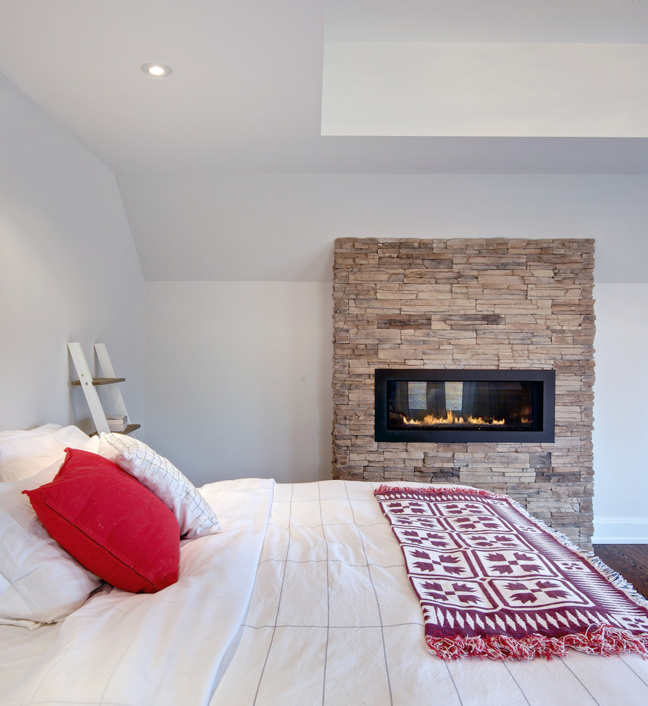 Imagen de dormitorio principal actual de tamaño medio con paredes grises, suelo de madera en tonos medios, todas las chimeneas y marco de chimenea de piedra
