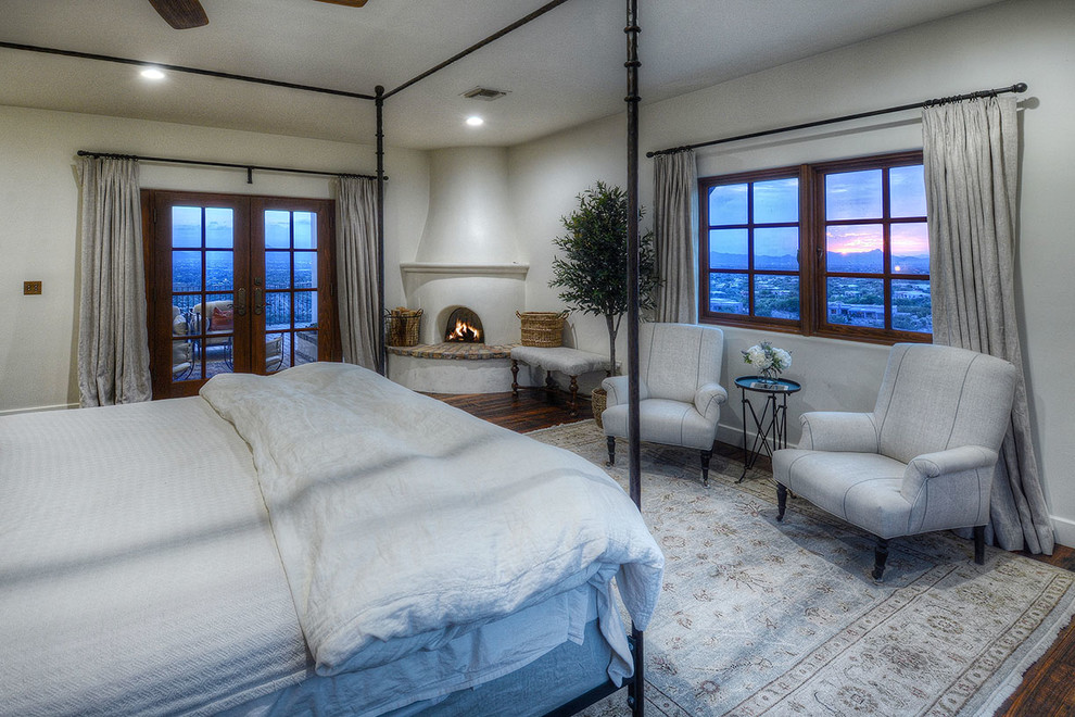フェニックスにある広い地中海スタイルのおしゃれな主寝室 (白い壁、濃色無垢フローリング、コーナー設置型暖炉、漆喰の暖炉まわり、茶色い床) のレイアウト