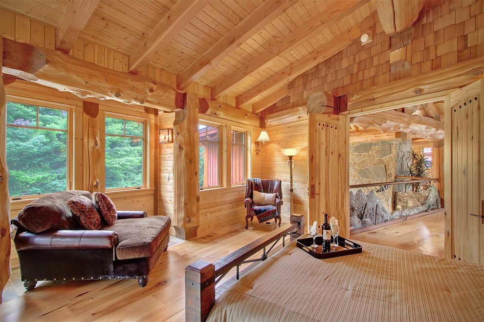 Foto de dormitorio principal rural grande con paredes marrones, suelo de madera clara, todas las chimeneas y marco de chimenea de piedra