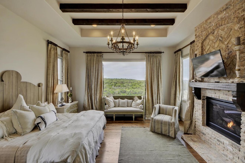 Inspiration for a mediterranean grey and brown bedroom in Austin with white walls, medium hardwood flooring, a standard fireplace, a stone fireplace surround and brown floors.