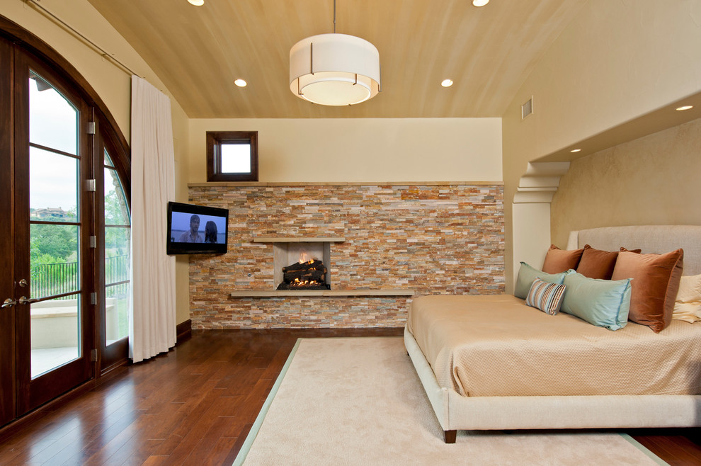Immagine di una camera da letto mediterranea con cornice del camino in pietra e TV