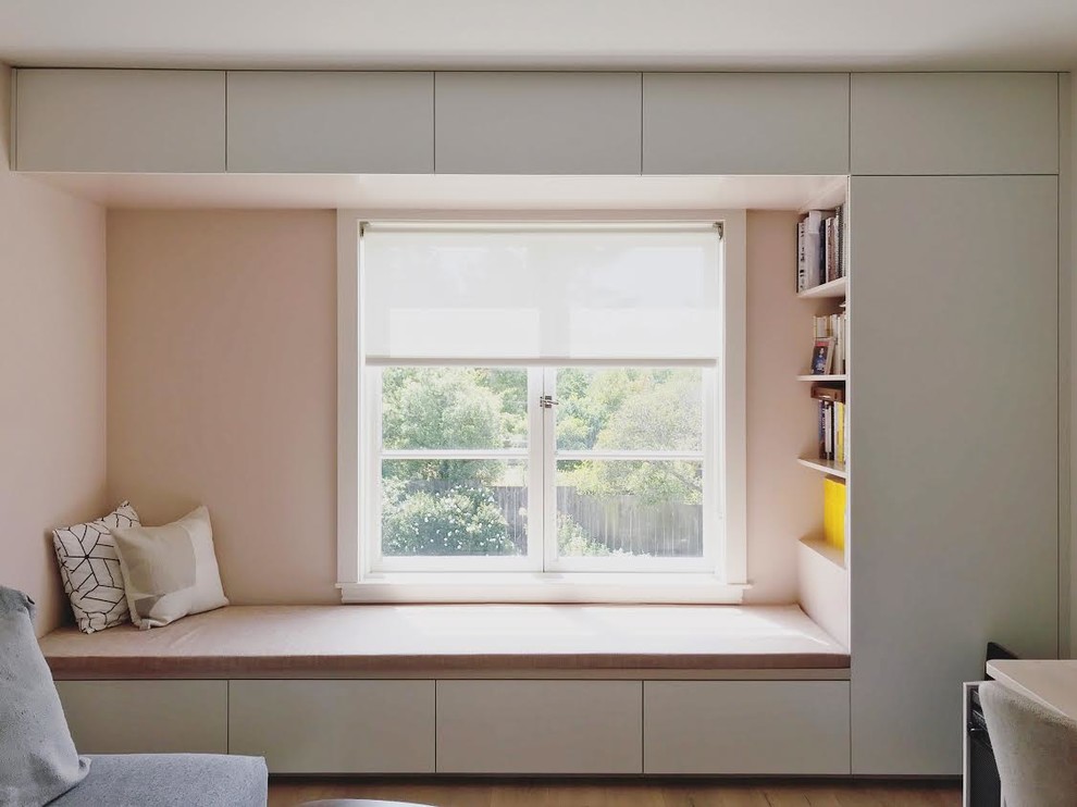 Modelo de dormitorio contemporáneo con paredes rosas, suelo de madera clara y suelo marrón
