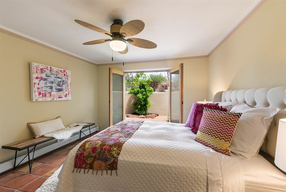 Ejemplo de dormitorio principal de estilo americano de tamaño medio sin chimenea con paredes amarillas, suelo de baldosas de terracota y suelo naranja
