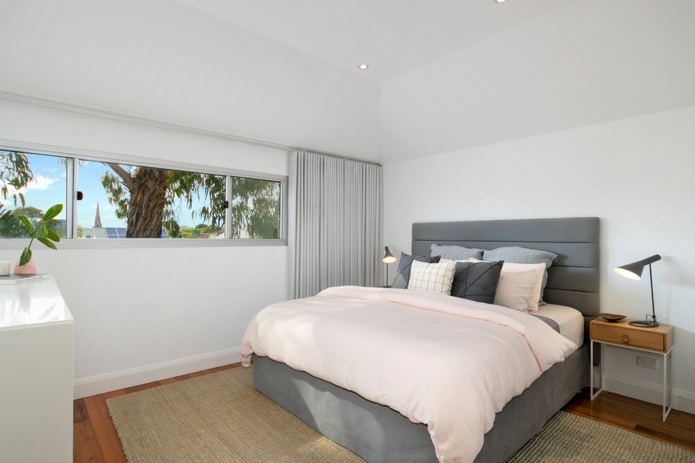 Diseño de dormitorio principal contemporáneo sin chimenea con suelo de madera en tonos medios, paredes blancas y suelo marrón