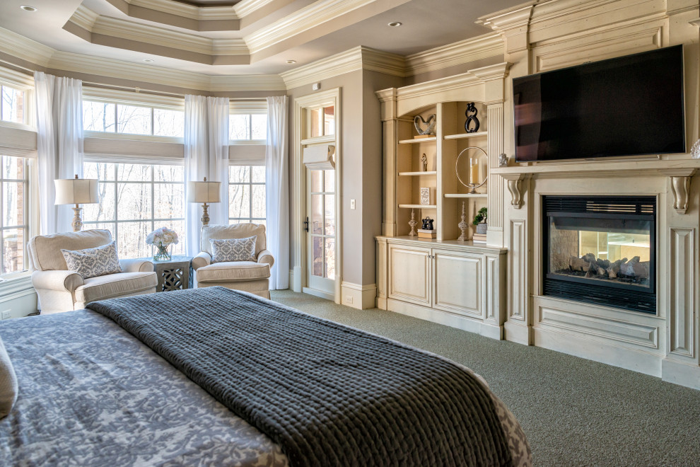 Geräumiges Hauptschlafzimmer mit grauer Wandfarbe, Teppichboden, Tunnelkamin, Kaminumrandung aus Holz, grauem Boden und eingelassener Decke in Raleigh