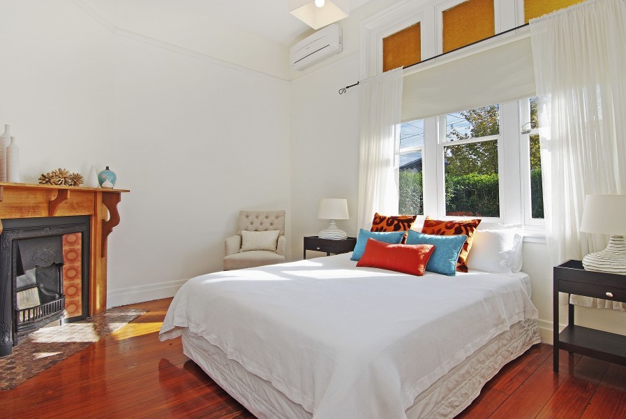 Ejemplo de dormitorio principal minimalista con paredes blancas, suelo de madera en tonos medios, chimenea de esquina, marco de chimenea de madera y suelo marrón