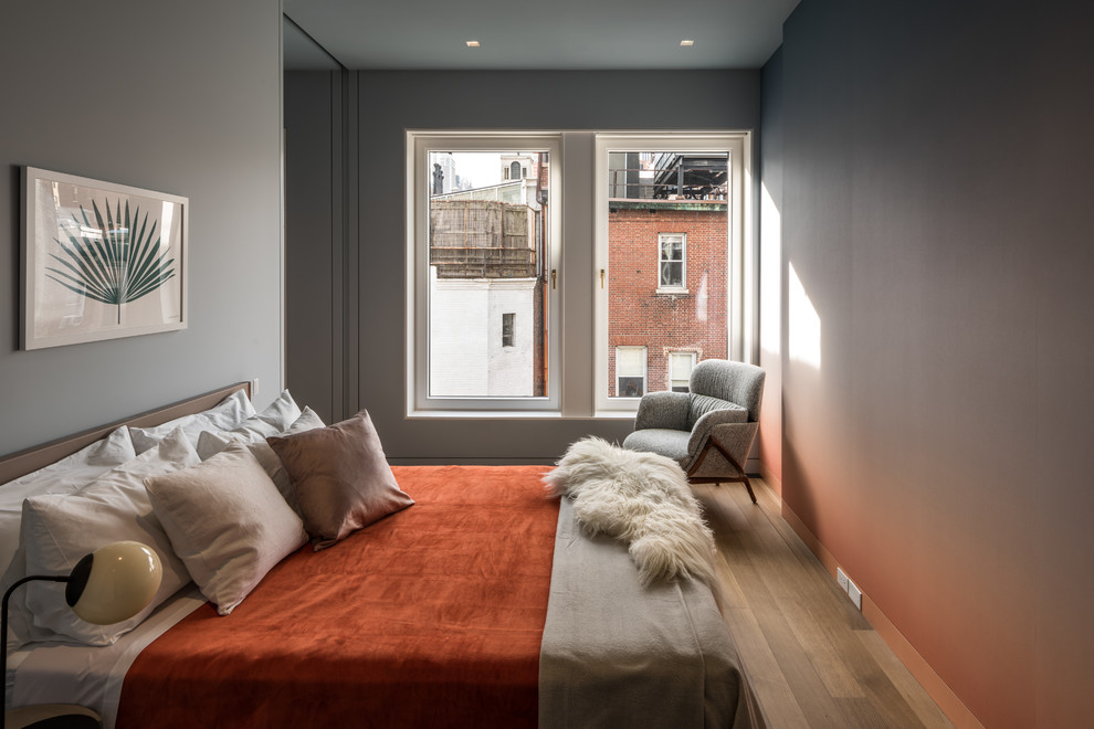 Example of a mid-sized trendy medium tone wood floor and brown floor bedroom design in New York with gray walls