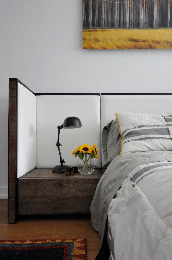 Cette image montre une chambre parentale minimaliste de taille moyenne avec un mur blanc et un sol en bois brun.