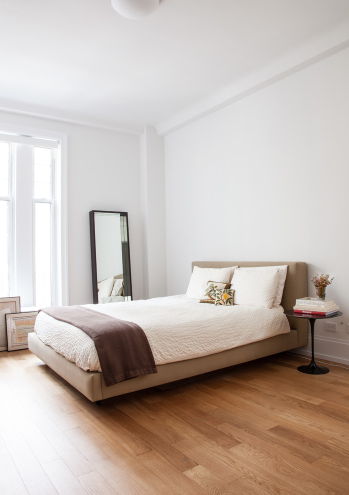 Exemple d'une chambre tendance avec un mur blanc et un sol en bois brun.