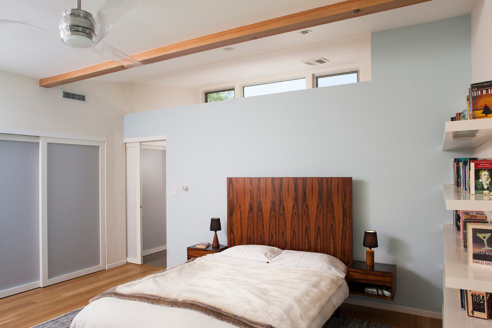 Modelo de dormitorio contemporáneo de tamaño medio sin chimenea con paredes azules y suelo de madera clara