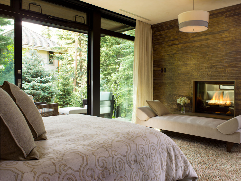 На фото: спальня в современном стиле с двусторонним камином и фасадом камина из камня