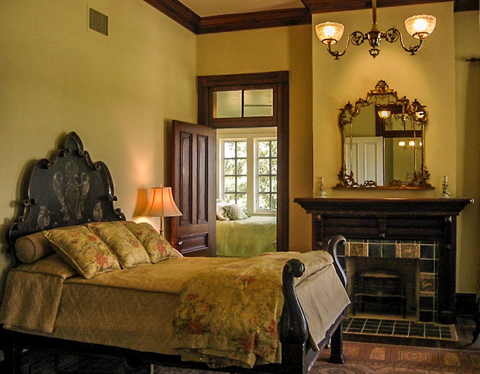 Modelo de dormitorio principal de estilo de casa de campo de tamaño medio con paredes beige, suelo de madera en tonos medios, todas las chimeneas y marco de chimenea de baldosas y/o azulejos