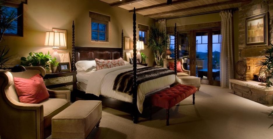 Ejemplo de dormitorio principal de estilo americano con paredes beige, moqueta, chimenea de esquina, marco de chimenea de piedra y suelo beige