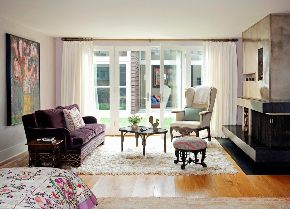 Cette image montre une grande chambre parentale bohème avec un manteau de cheminée en béton, un mur violet, parquet clair et une cheminée d'angle.