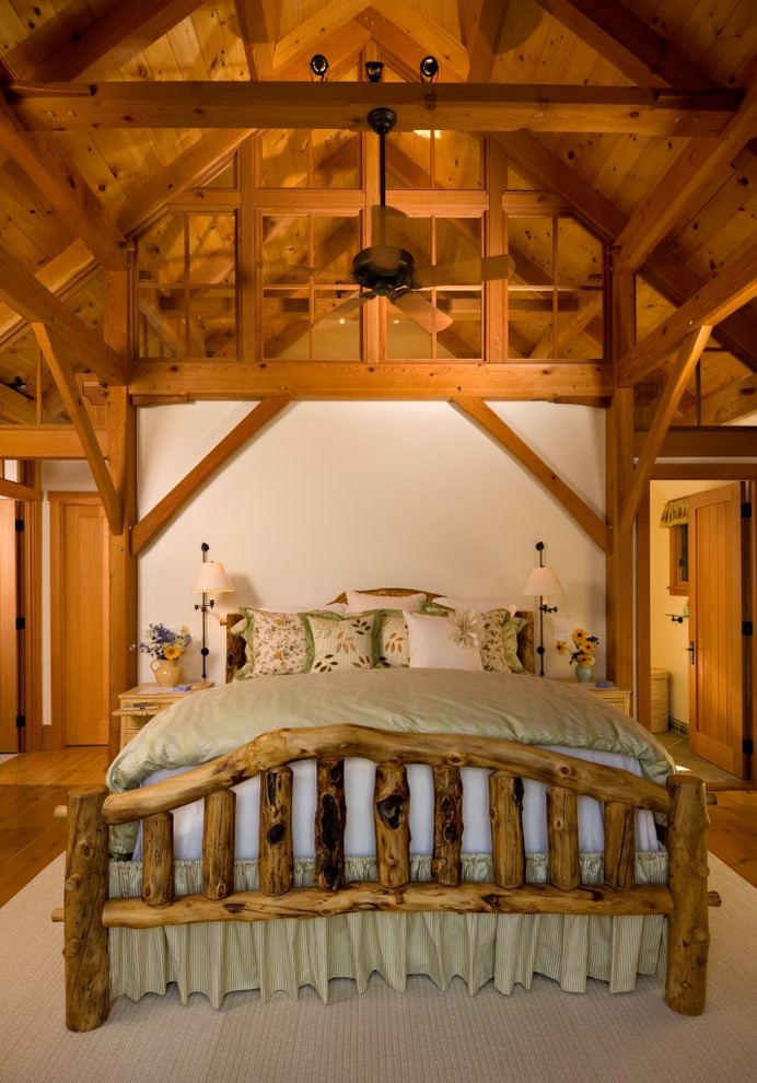 Modelo de dormitorio principal rural grande con paredes beige, suelo de madera clara, todas las chimeneas, marco de chimenea de piedra y suelo beige