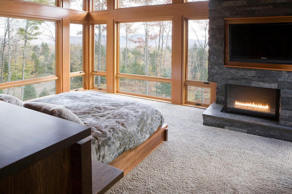 Example of a large mountain style master carpeted bedroom design in Other with a corner fireplace, a stone fireplace and gray walls