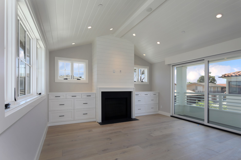 Großes Landhausstil Hauptschlafzimmer mit grauer Wandfarbe, hellem Holzboden, Kamin, Kaminumrandung aus Holz und braunem Boden in Orange County