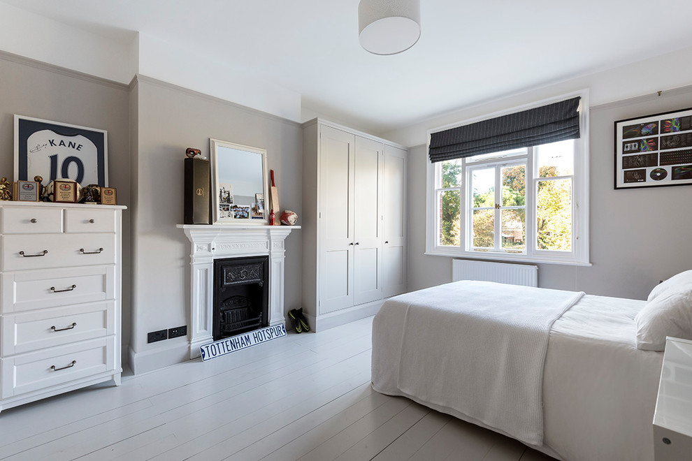 Klassisches Schlafzimmer mit grauer Wandfarbe, gebeiztem Holzboden, Kamin, Kaminumrandung aus Metall und grauem Boden in Sonstige