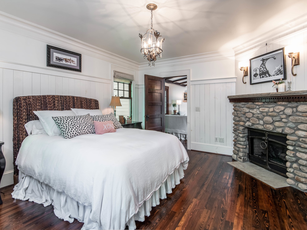 Photo of a medium sized country master bedroom in Other with white walls, dark hardwood flooring, a standard fireplace, a stone fireplace surround and brown floors.