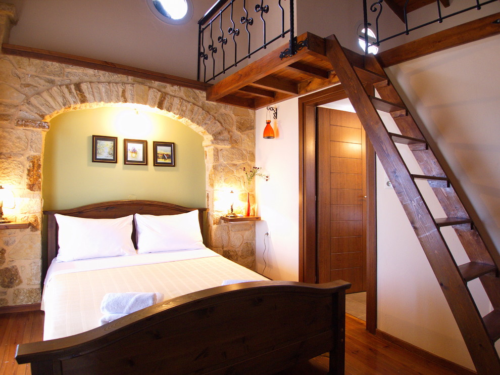 Imagen de dormitorio tipo loft marinero de tamaño medio con suelo de madera oscura, chimenea de esquina y marco de chimenea de piedra
