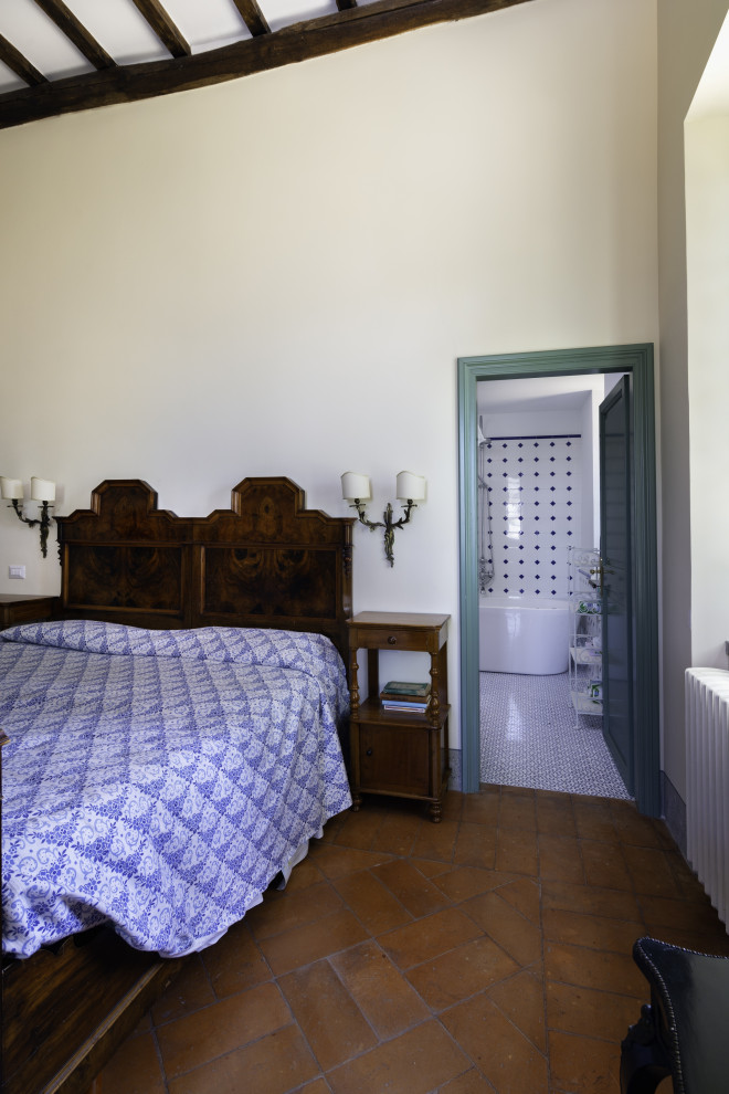 Foto di un'ampia camera matrimoniale tradizionale con pareti bianche, pavimento in mattoni, camino classico, cornice del camino in pietra e pavimento marrone
