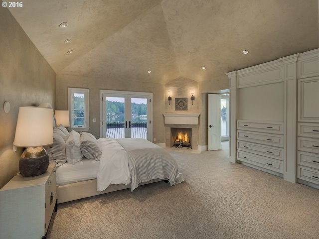 This is an example of an expansive mediterranean master bedroom in Portland with beige walls, carpet, a corner fireplace, a stone fireplace surround, beige floors and feature lighting.