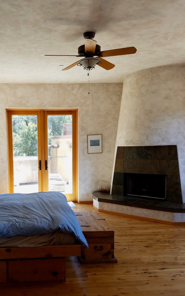 他の地域にある広い地中海スタイルのおしゃれな主寝室 (ベージュの壁、無垢フローリング、標準型暖炉、漆喰の暖炉まわり、茶色い床) のインテリア
