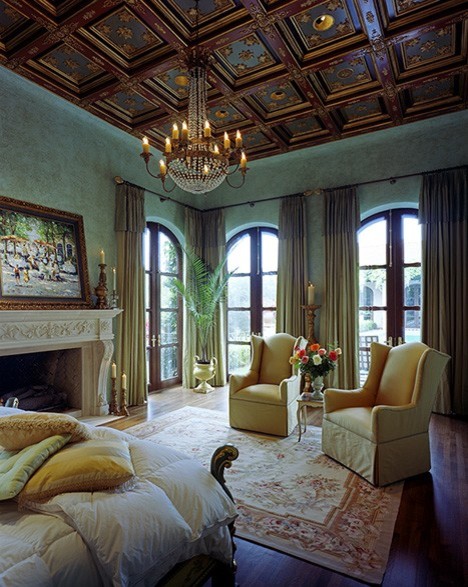 Foto di una grande camera matrimoniale mediterranea con pareti verdi, pavimento in legno massello medio, camino classico, cornice del camino in pietra e pavimento marrone