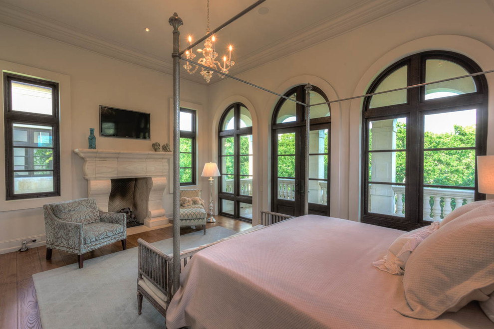 Imagen de dormitorio principal con paredes blancas, suelo de madera en tonos medios, todas las chimeneas y marco de chimenea de piedra