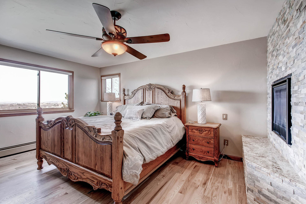 Imagen de dormitorio principal tradicional de tamaño medio con paredes beige, suelo de madera clara, chimenea de doble cara y marco de chimenea de ladrillo