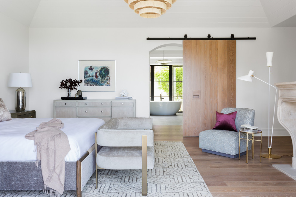 Geräumiges Modernes Hauptschlafzimmer mit weißer Wandfarbe, braunem Holzboden, Kamin, Kaminumrandung aus Stein und beigem Boden in Houston