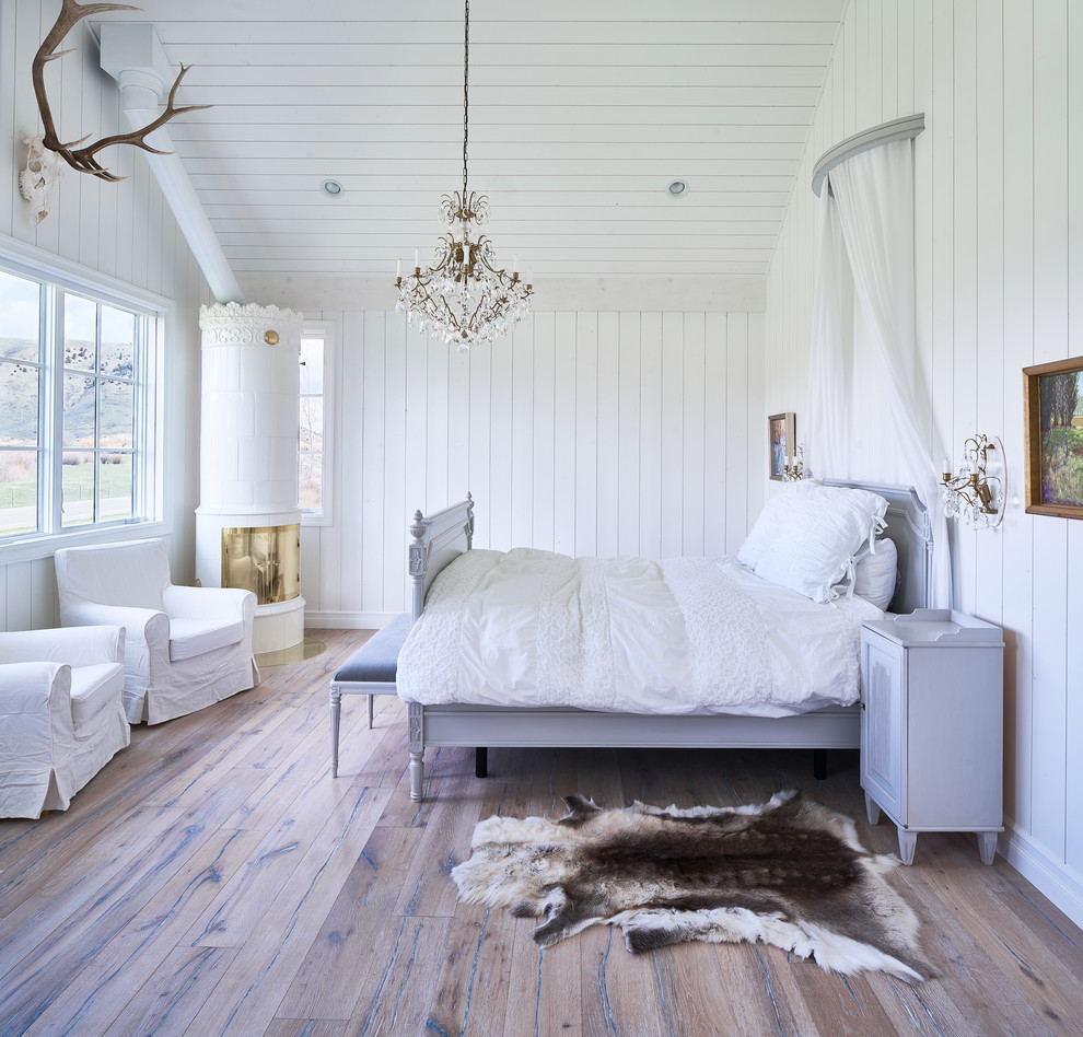 Modelo de dormitorio campestre con paredes blancas, suelo de madera oscura, estufa de leña y marco de chimenea de metal