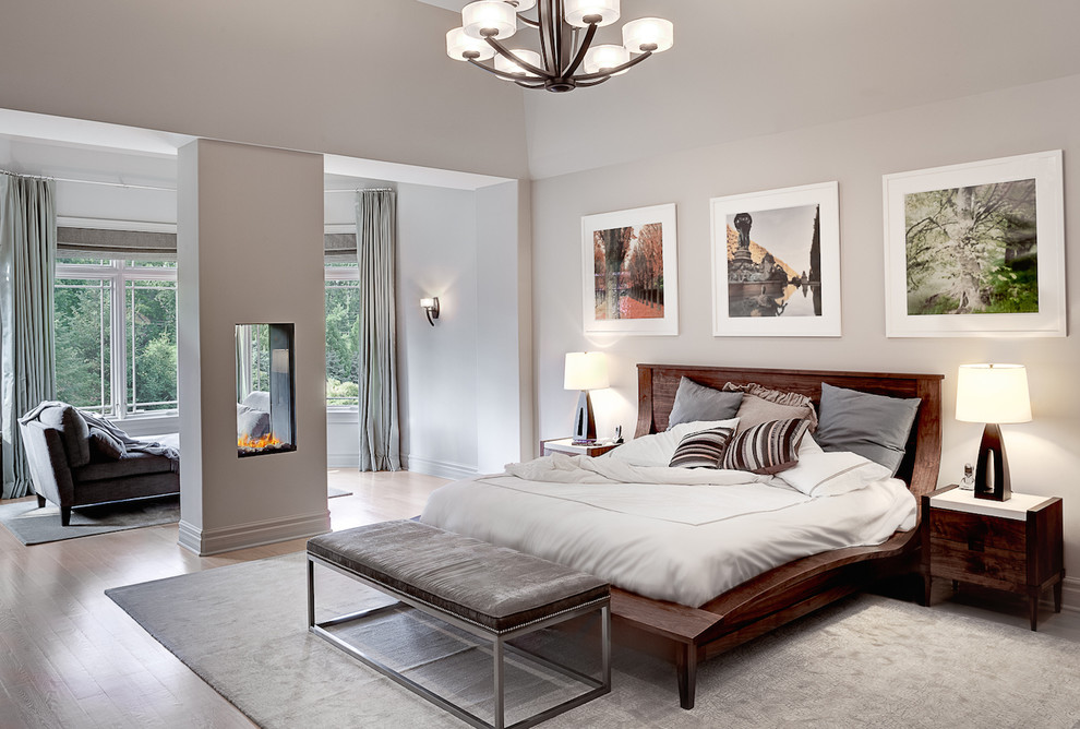 На фото: хозяйская спальня в современном стиле с серыми стенами, паркетным полом среднего тона и двусторонним камином