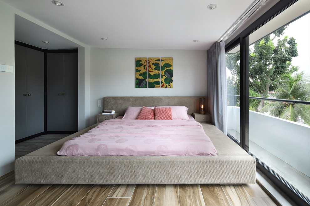 Photo of a world-inspired master and grey and pink bedroom in Singapore with white walls, medium hardwood flooring and beige floors.