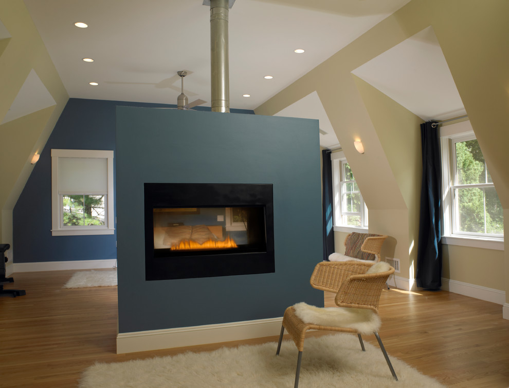 Bild på ett stort minimalistiskt huvudsovrum, med blå väggar, ljust trägolv, en dubbelsidig öppen spis och en spiselkrans i gips