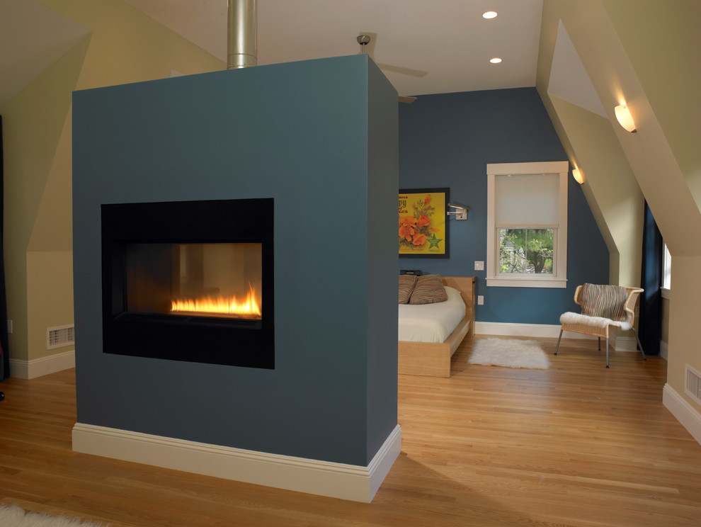 Cette photo montre une grande chambre parentale scandinave avec un mur bleu, parquet clair, une cheminée double-face et un manteau de cheminée en plâtre.