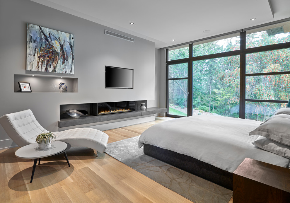 Imagen de dormitorio principal actual con paredes grises, suelo de madera clara y chimenea lineal