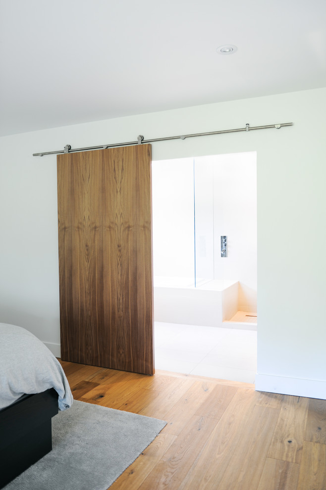 Imagen de dormitorio principal minimalista con paredes blancas, suelo de madera en tonos medios y suelo marrón