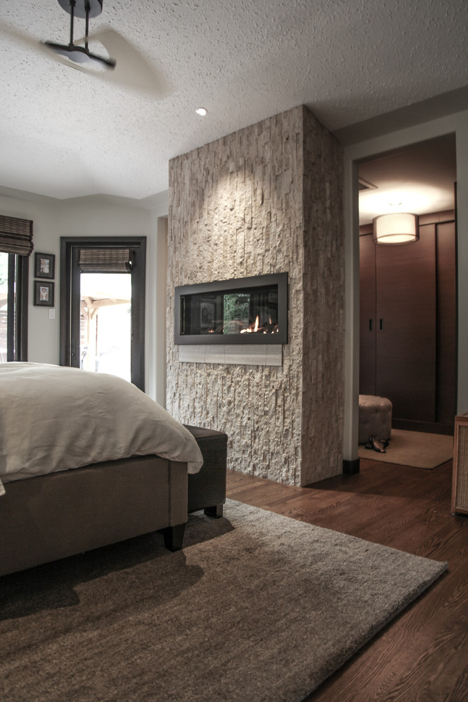 Idée de décoration pour une chambre parentale design de taille moyenne avec un manteau de cheminée en pierre, un sol en bois brun et une cheminée ribbon.