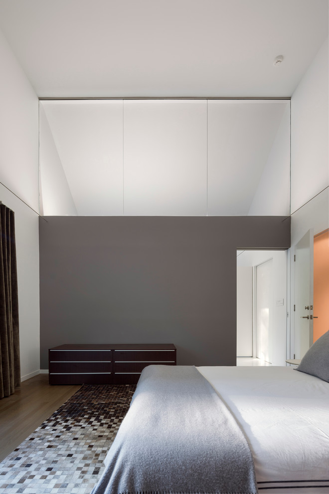 Cette photo montre une grande chambre tendance avec un mur gris, un sol en bois brun et un sol marron.